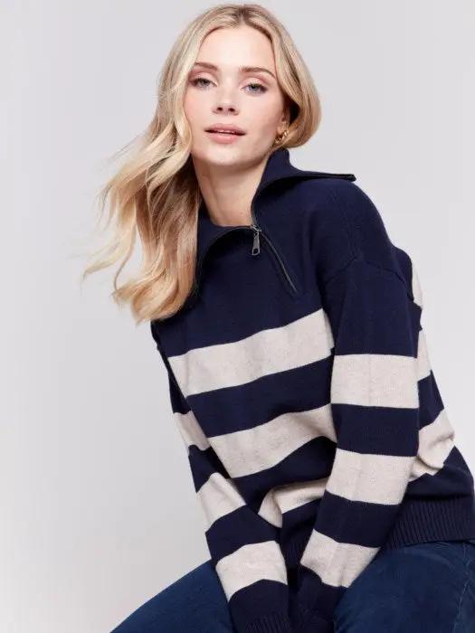A person with light-colored hair wears a high-quality Charlie B Striped Turtleneck with Side Zip in navy and white, paired with dark pants against a plain background.
