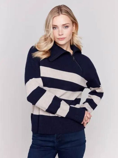 A person with light-colored hair wears a high-quality Charlie B Striped Turtleneck with Side Zip in navy and white, paired with dark pants against a plain background.
