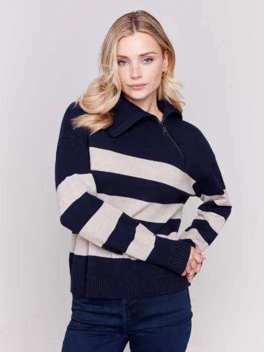 A person with light-colored hair wears a high-quality Charlie B Striped Turtleneck with Side Zip in navy and white, paired with dark pants against a plain background.
