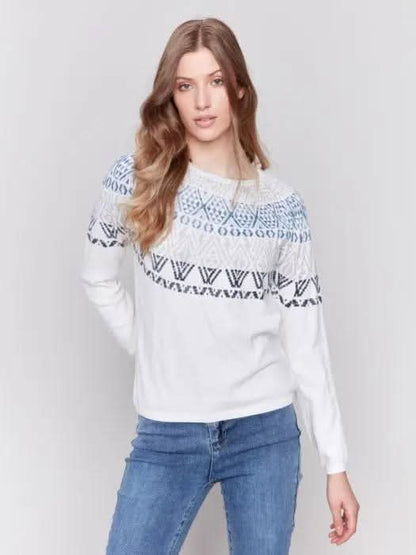 A person dons a Charlie B Ecru Ski Sweater and blue jeans, standing in a studio setting with a plain background, epitomizing ultimate comfort for winter adventures.