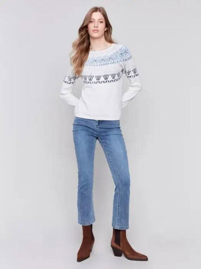 A person dons a Charlie B Ecru Ski Sweater and blue jeans, standing in a studio setting with a plain background, epitomizing ultimate comfort for winter adventures.