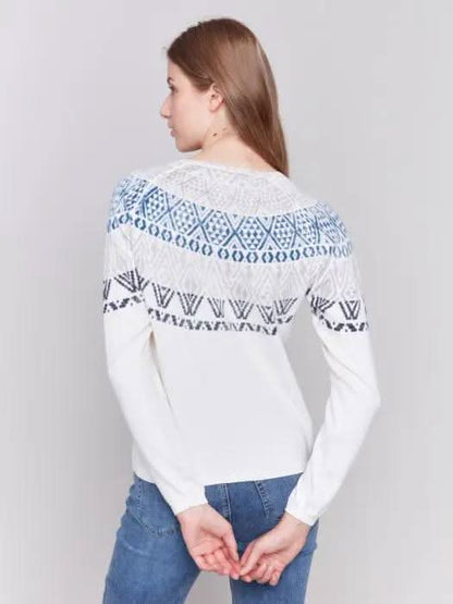 A person dons a Charlie B Ecru Ski Sweater and blue jeans, standing in a studio setting with a plain background, epitomizing ultimate comfort for winter adventures.
