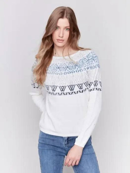 A person dons a Charlie B Ecru Ski Sweater and blue jeans, standing in a studio setting with a plain background, epitomizing ultimate comfort for winter adventures.