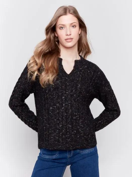 A person with long hair wearing the black Sparkled Yarn Cable Sweater from Charlie B, crafted from ultra-soft material, paired with blue jeans stands against a plain background, looking at the camera.