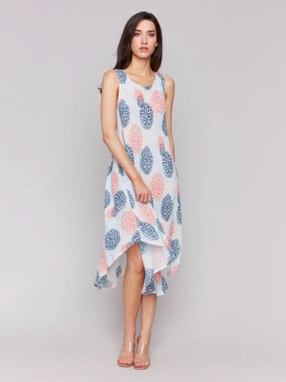 Against a plain backdrop, someone showcases Charlie B’s Sleeveless Printed Rayon Dress, featuring breathable rayon fabric and a charming blue and pink floral pattern with an asymmetrical hemline.