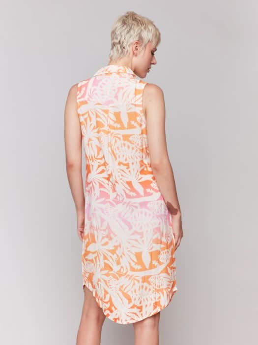 A person with short blonde hair wears the Charlie B Printed Sleeveless Button-Front Dress with a pink and orange leaf pattern and beige heels, standing against a plain light background.