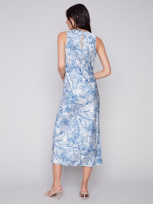 A woman in a blue and white jungle print Charlie B sleeveless long satin dress, standing against a light gray background. She is wearing light sandals.