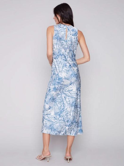 A woman in a blue and white jungle print Charlie B sleeveless long satin dress, standing against a light gray background. She is wearing light sandals.