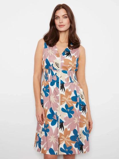 A woman stands against a white wall wearing the Charlie B Cotton Voile Printed Front-Zip Dress and brown sandals.