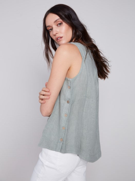 A person in a Charlie B Sleeveless Linen Top with Side Buttons and white pants stands against a plain background.