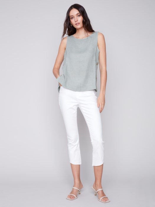A person in a Charlie B Sleeveless Linen Top with Side Buttons and white pants stands against a plain background.