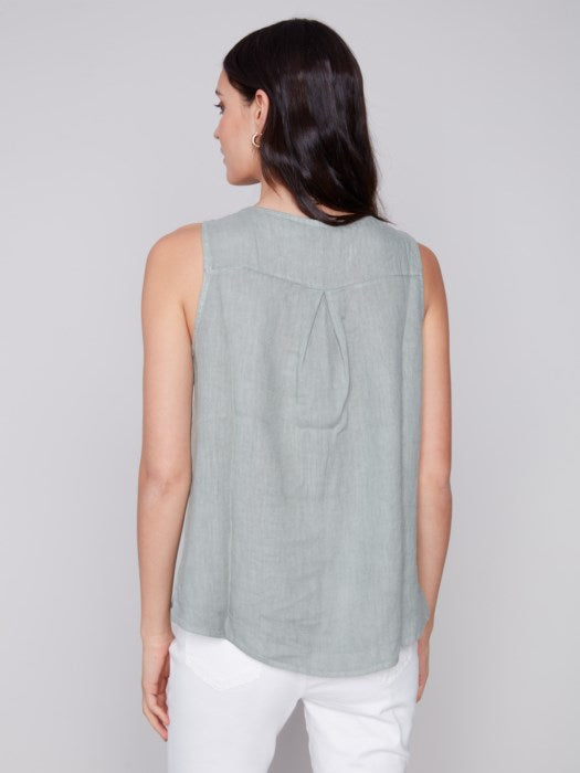 A person in a Charlie B Sleeveless Linen Top with Side Buttons and white pants stands against a plain background.