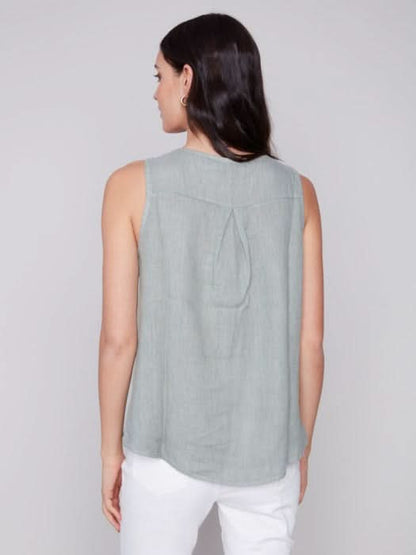 A person in a Charlie B Sleeveless Linen Top with Side Buttons and white pants stands against a plain background.