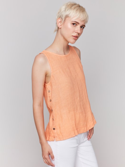 A person in a Charlie B Sleeveless Linen Top with Side Buttons and white pants stands against a plain background.