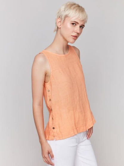 A person in a Charlie B Sleeveless Linen Top with Side Buttons and white pants stands against a plain background.