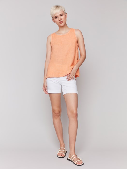A person in a Charlie B Sleeveless Linen Top with Side Buttons and white pants stands against a plain background.