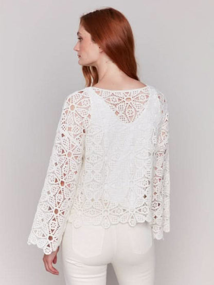A person with long hair, draped in a Charlie B Cotton Blend Crochet Top and white pants, stands gracefully against a neutral backdrop.