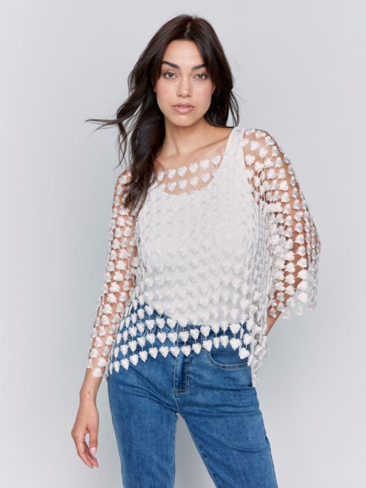 Against a plain backdrop, someone wears Charlie B's Textured Crochet Heart Top, a sheer pink heart-patterned piece layered over a white shirt.