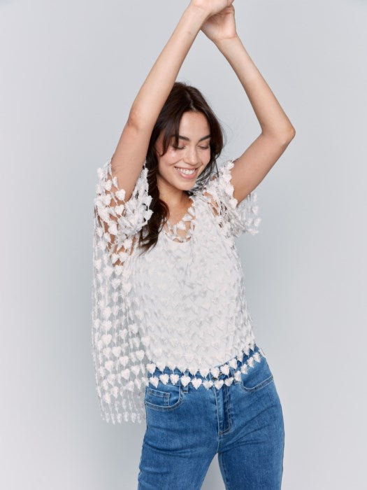 Against a plain backdrop, someone wears Charlie B's Textured Crochet Heart Top, a sheer pink heart-patterned piece layered over a white shirt.