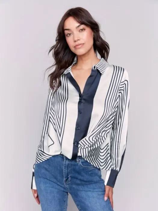 A woman wearing the Satin Twisted Detail Front Shirt by Charlie B along with jeans stands against a plain background. Her long brown hair complements the ensemble, giving her an elegant look, while she maintains a neutral expression.