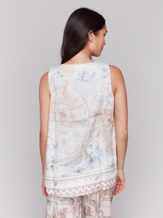 A woman with long hair wears a Charlie B Printed Sleeveless Linen Blend Top and light-patterned pants against a plain gray background, the boat neck top adding elegance to the minimalist setting.