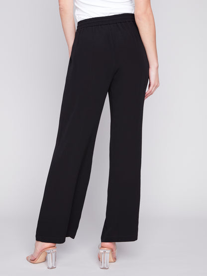 A woman wearing stylish Charlie B black satin wide-leg pants and a white t-shirt.