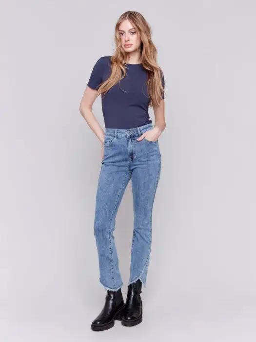 A person wearing Charlie B's light blue Front Tulip Hem Jeans, featuring frayed hem detailing, and black platform boots stands against a light background, showcasing their unique design.