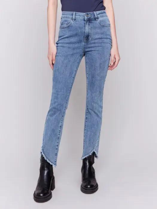 A person wearing Charlie B's light blue Front Tulip Hem Jeans, featuring frayed hem detailing, and black platform boots stands against a light background, showcasing their unique design.