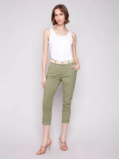 A woman stands against a plain background wearing a white sleeveless top, Charlie B Slim Fit Pants with Belt in celadon green stretch cotton, and nude high-heeled sandals.