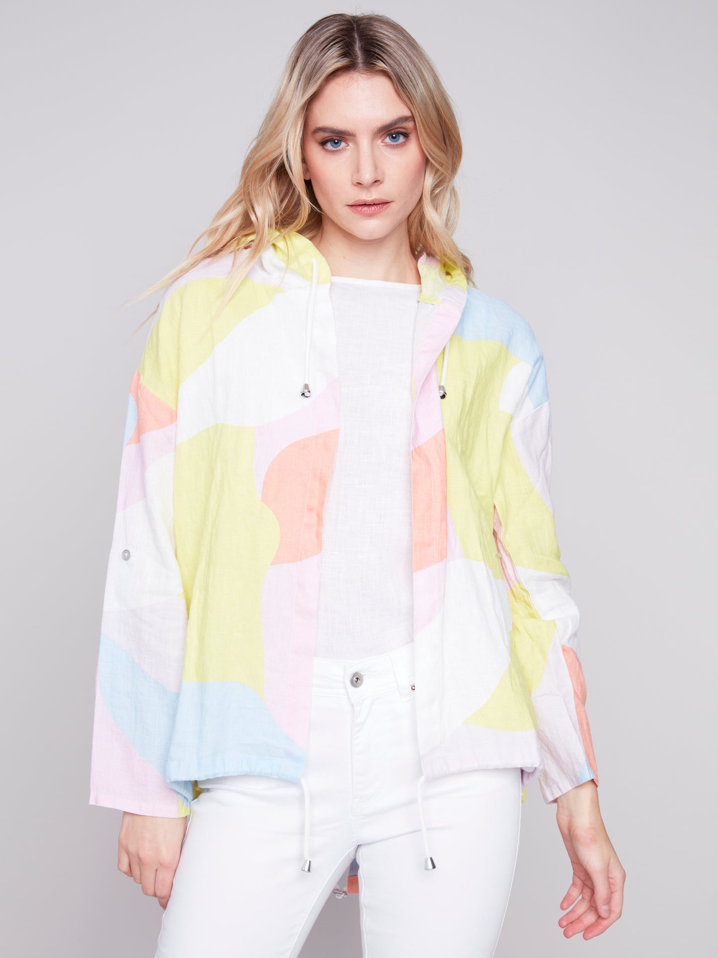 Woman wearing a Charlie B Graffiti Duster Jacket and white pants against a grey background.