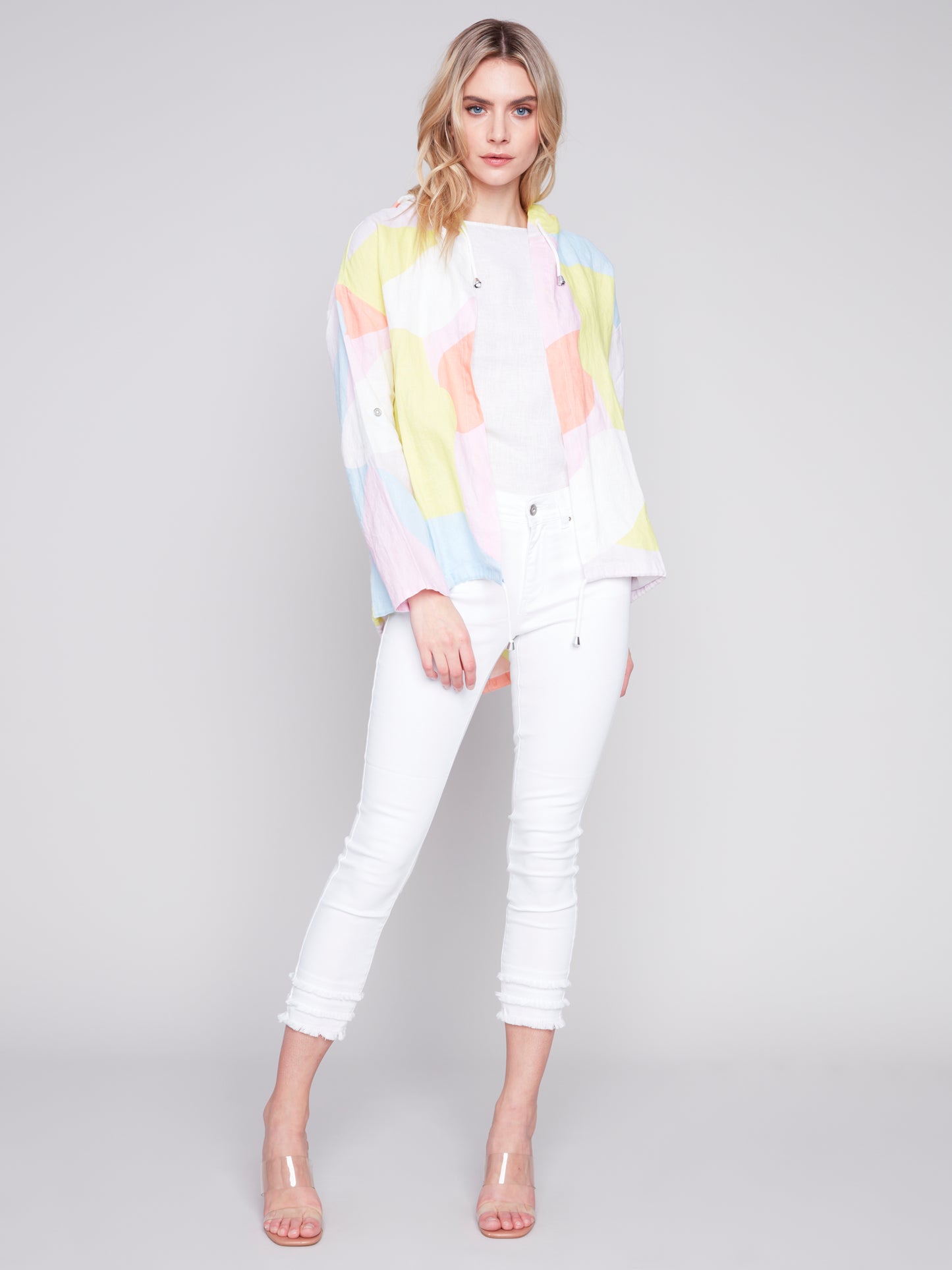 Woman wearing a Charlie B Graffiti Duster Jacket and white pants against a grey background.