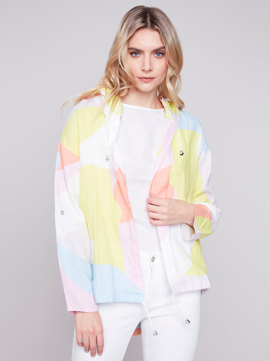 Woman wearing a Charlie B Graffiti Duster Jacket and white pants against a grey background.