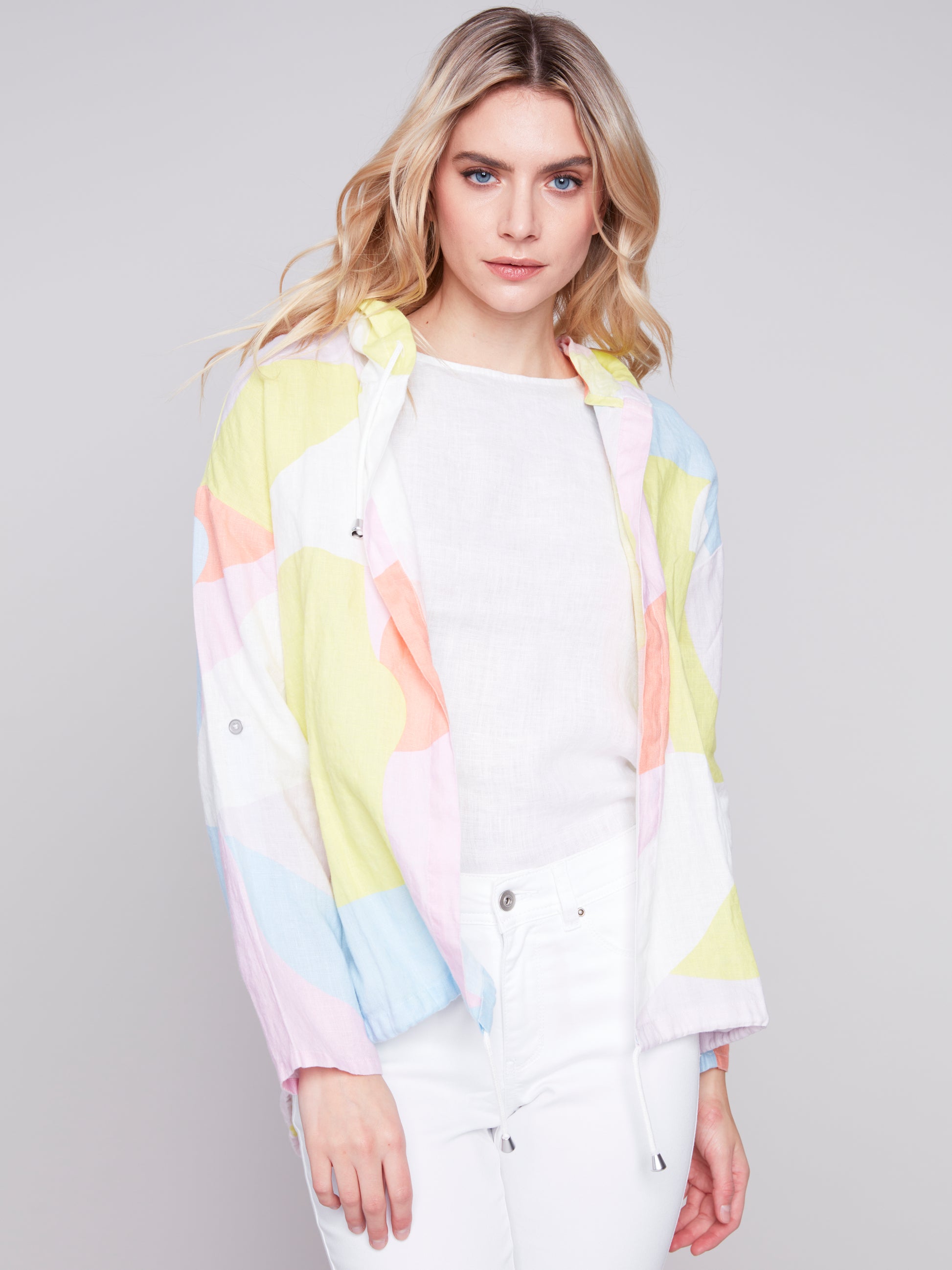 Woman wearing a Charlie B Graffiti Duster Jacket and white pants against a grey background.