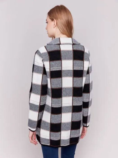 A woman with long hair, standing against a plain background and showcasing her winter wardrobe, is wearing the Charlie B Knit Plaid Coat along with jeans.