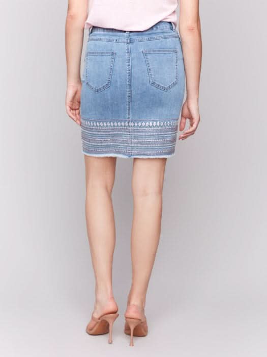 A person wears a light pink top and the Charlie B Embroidered Hem Denim Skort, paired with nude heeled sandals, standing against a plain background.