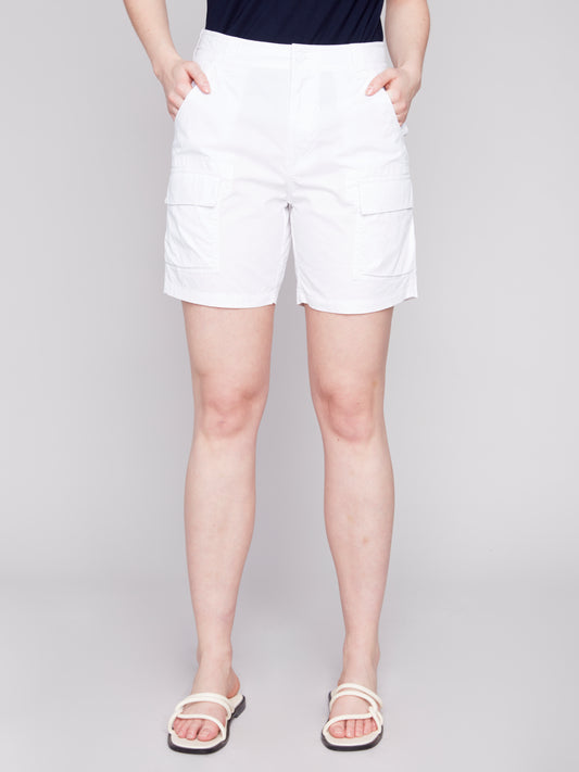A woman stands wearing a navy tank top and stylish Charlie B Cargo Pocket Cotton Shorts with white sandals against a light gray background.