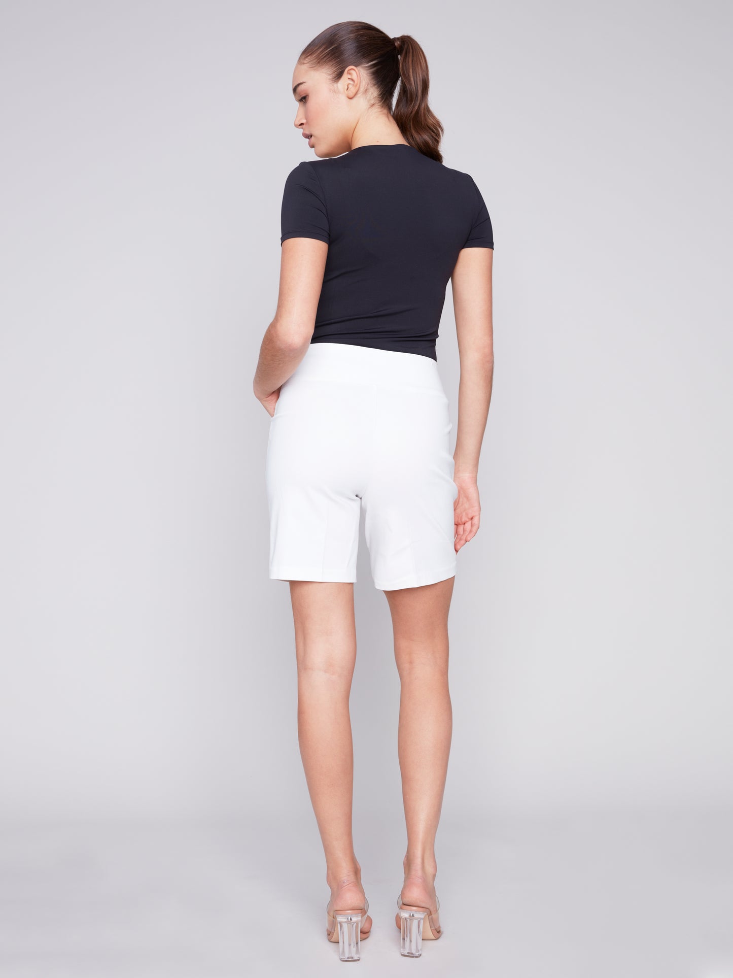 A woman wearing Charlie B smooth stretch shorts in black, paired with a stylish white top, showcasing both comfort and style.