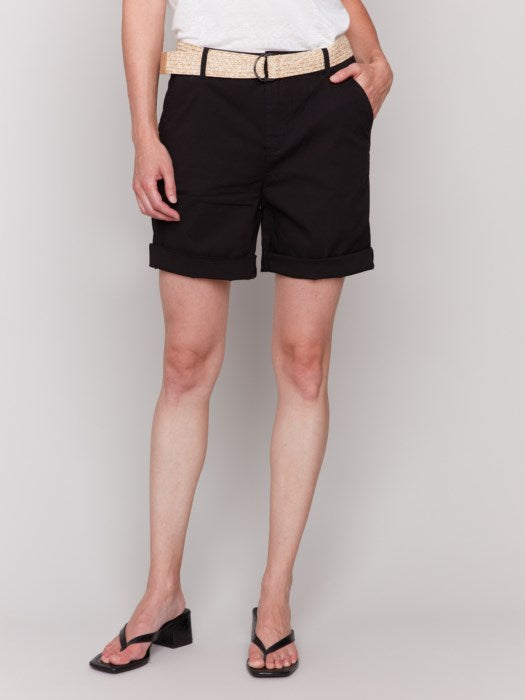 A fashionista against a plain background wears chic Charlie B Cuffed Shorts with a light belt, a crisp white top, and stylish black sandals.