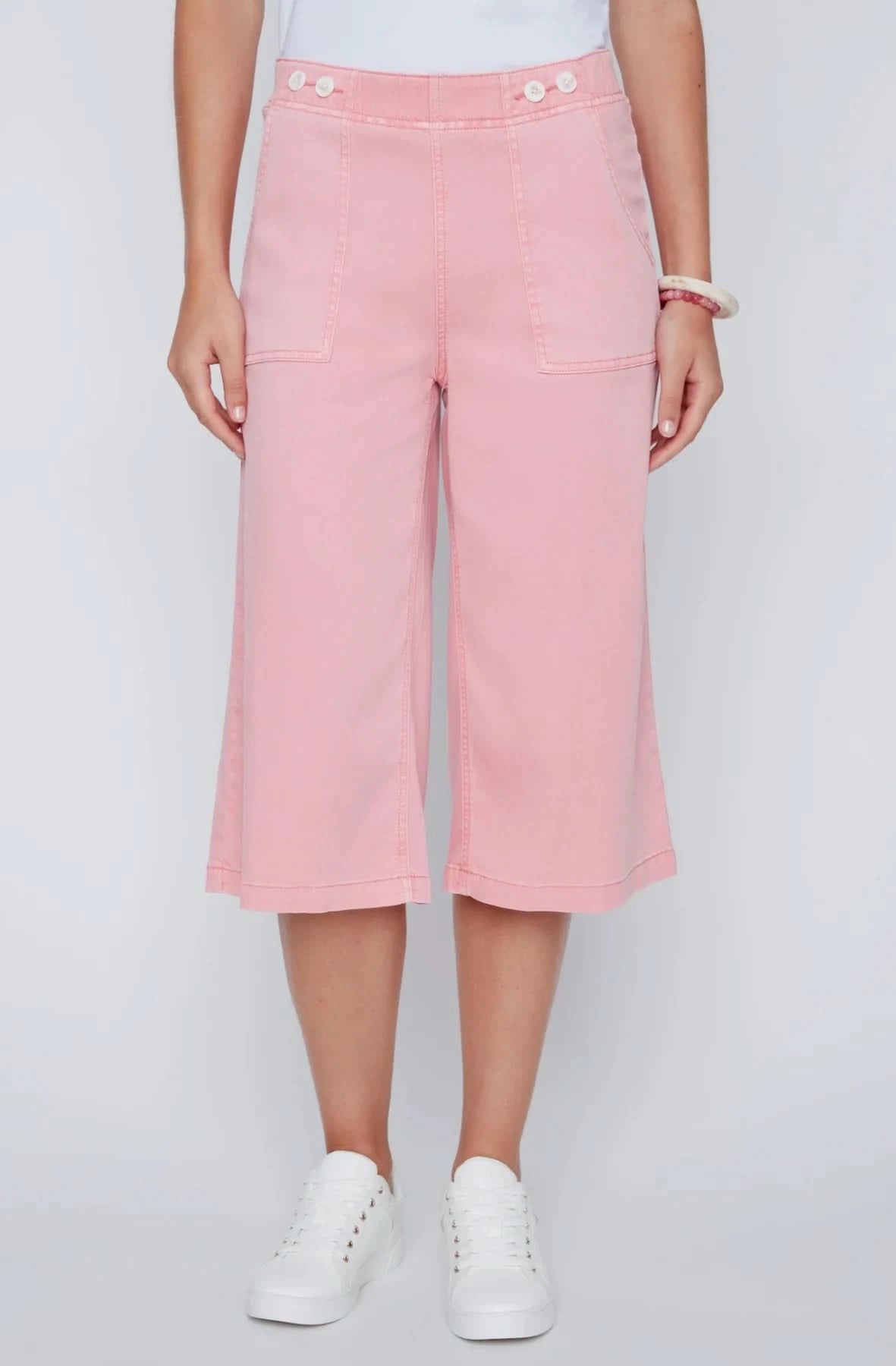 A woman stands against a plain background wearing a white sleeveless top, CoCo Y Club wide-leg cropped pants in light pink Capri Gaucho style, and white sneakers—a perfect addition to any casual wardrobe.