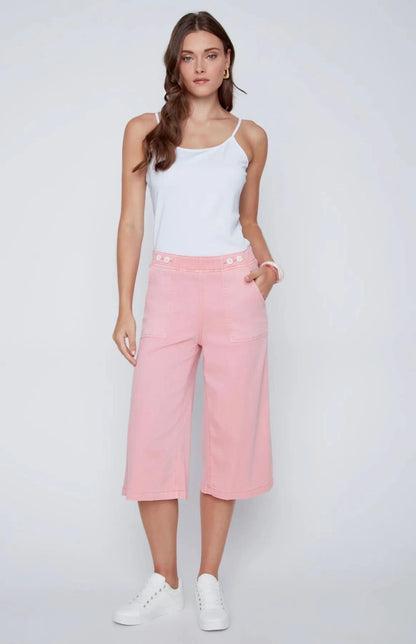 A woman stands against a plain background wearing a white sleeveless top, CoCo Y Club wide-leg cropped pants in light pink Capri Gaucho style, and white sneakers—a perfect addition to any casual wardrobe.