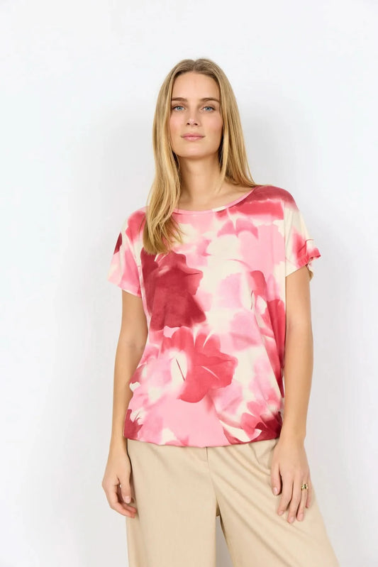 A woman faces away, wearing the pink and white tie-dye Marica Top by Soya Concepts with beige wide-leg pants, set against a plain white background.