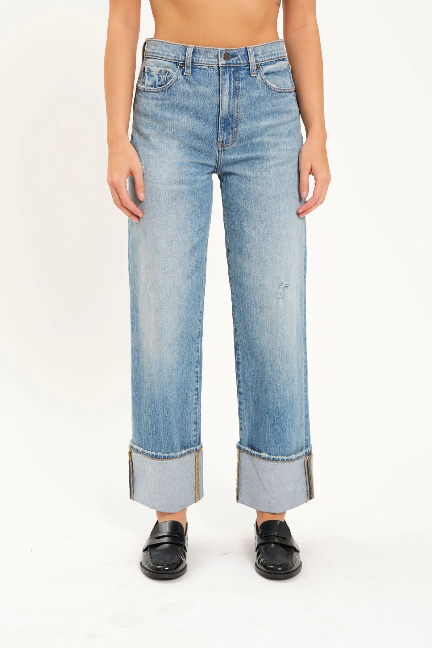 A person is wearing the Eastside High Rise Loose with Wide Cuff jeans in blue, made from organic cotton by Daze, paired with black loafers. The upper body is not shown.
