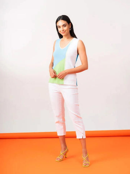 A woman poses on an orange surface, displaying a Multi Color Tank Top by Elena Wang with green, blue, and white sections. She pairs it with comfortable white capri pants and yellow sandals—perfect for everyday wear—set against a neutral background.
