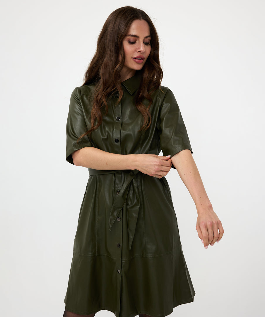 A woman in a sexy and trendy green Front Tie Leather Dress from Esqualo stands sideways with her head tilted slightly forward, her eyes closed, and her hand near her face against a plain white background.