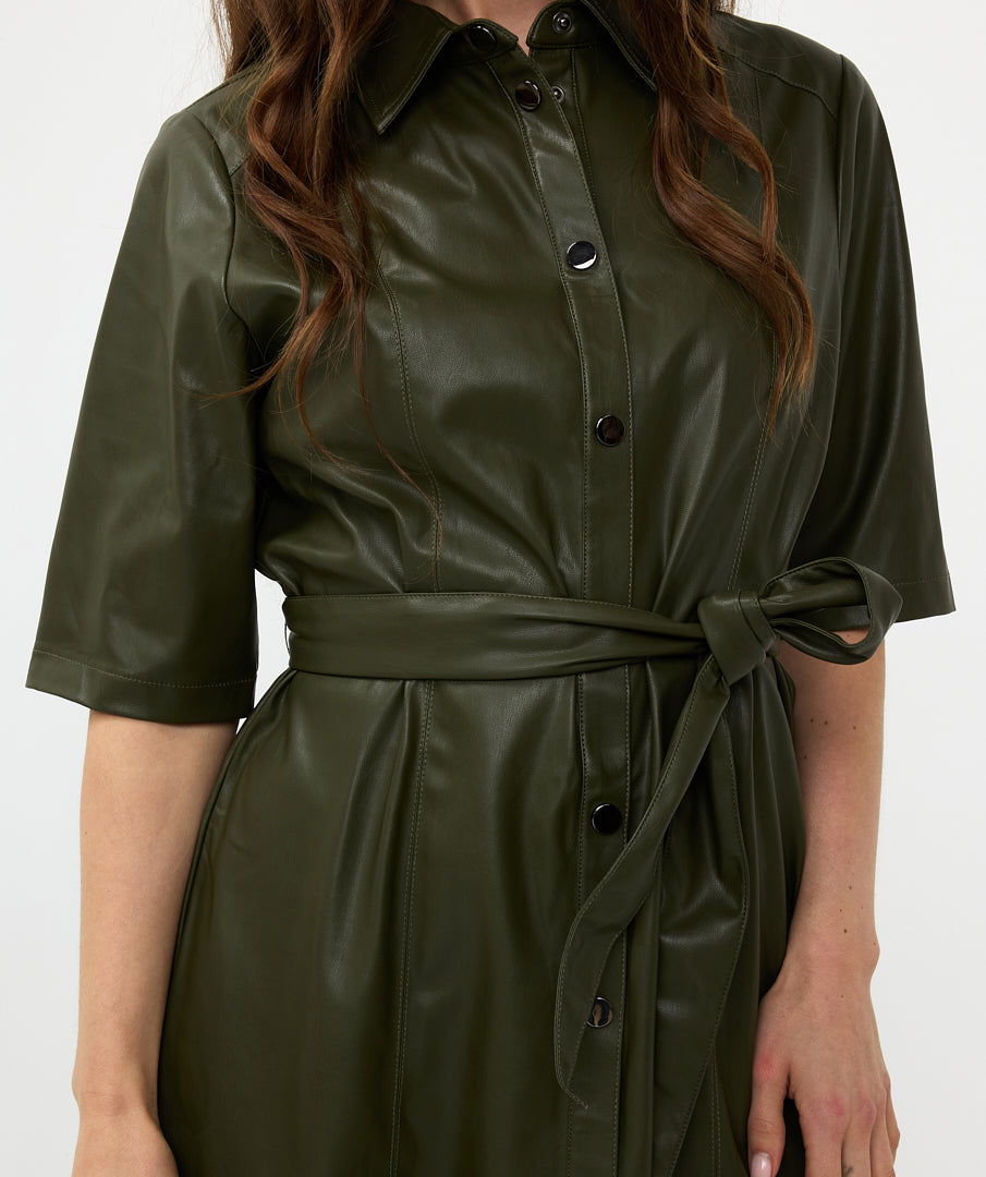 A woman in a sexy and trendy green Front Tie Leather Dress from Esqualo stands sideways with her head tilted slightly forward, her eyes closed, and her hand near her face against a plain white background.