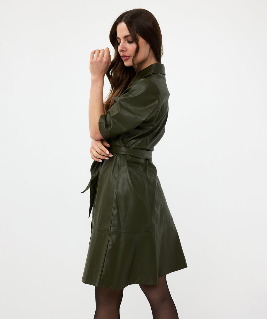 A woman in a sexy and trendy green Front Tie Leather Dress from Esqualo stands sideways with her head tilted slightly forward, her eyes closed, and her hand near her face against a plain white background.