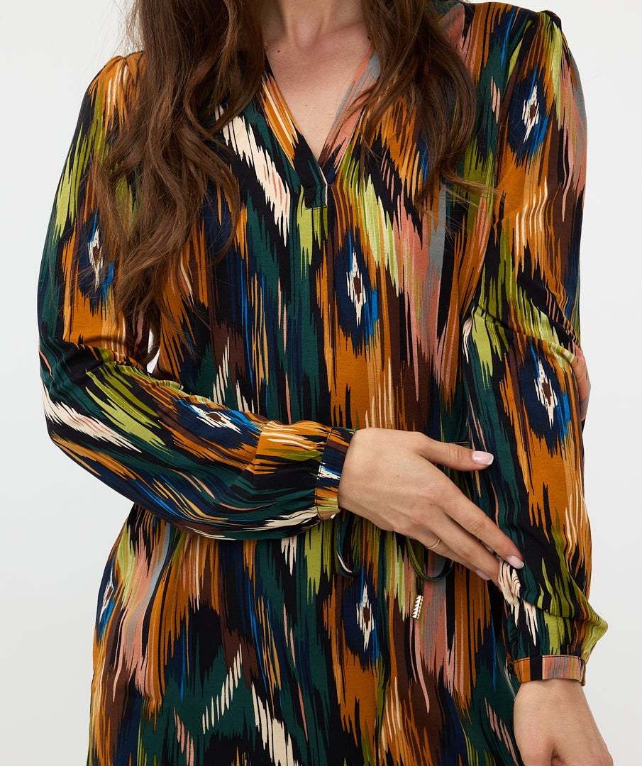 Wearing the versatile and stylish V-Neck Amazon Dress by Esqualo, this person pairs the vibrant, multicolored patterned garment with classic brown boots against a clean white background.