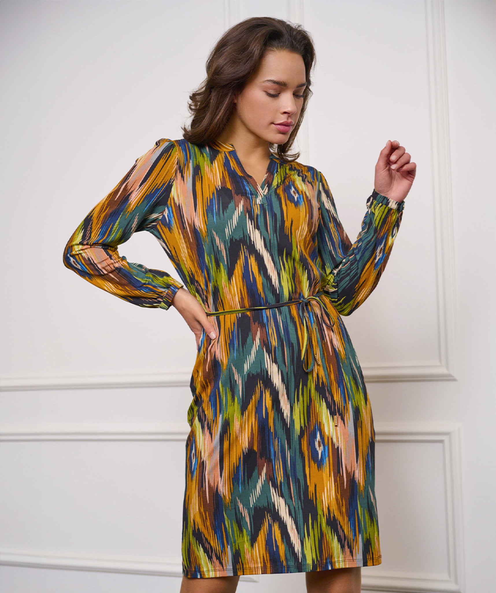 Wearing the versatile and stylish V-Neck Amazon Dress by Esqualo, this person pairs the vibrant, multicolored patterned garment with classic brown boots against a clean white background.
