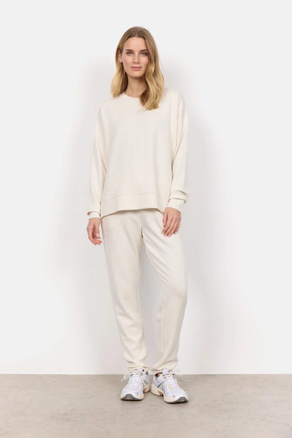 Wearing the Soya Concepts Banu Long Sleeve Sweater in off-white, paired with matching pants, this individual showcases relaxed style and all-day comfort against a simple backdrop.