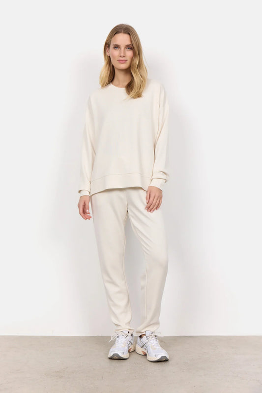 Wearing the Soya Concepts Banu Long Sleeve Sweater in off-white, paired with matching pants, this individual showcases relaxed style and all-day comfort against a simple backdrop.